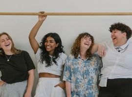 a group of friends standing in front of a white wall all laughing and looking at each other