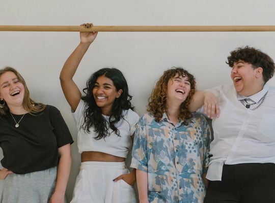 a group of friends standing in front of a white wall all laughing and looking at each other