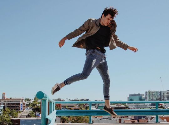 man mid-jump off a railing on top of a building on a cloudless day