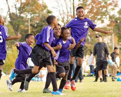 Four young kids in purple football kits celebrating a goal