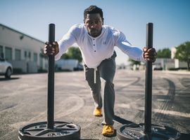 Man pushing a sled with weights in car park, head sweats