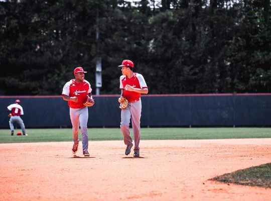 2 Baseball players between plays jog and chat at the same time. 