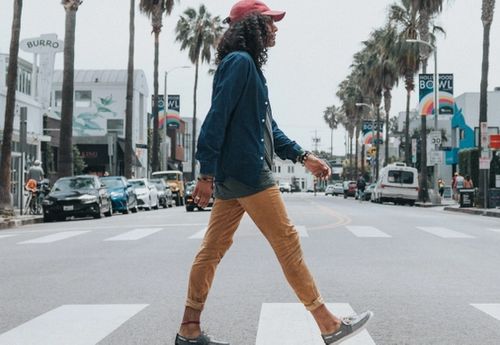 Man in a red baseball cap and long sleeve shirt and trousers, crossing the road