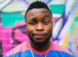 A man smiling with his eyebrow raised standing in front of a colorful graffiti background