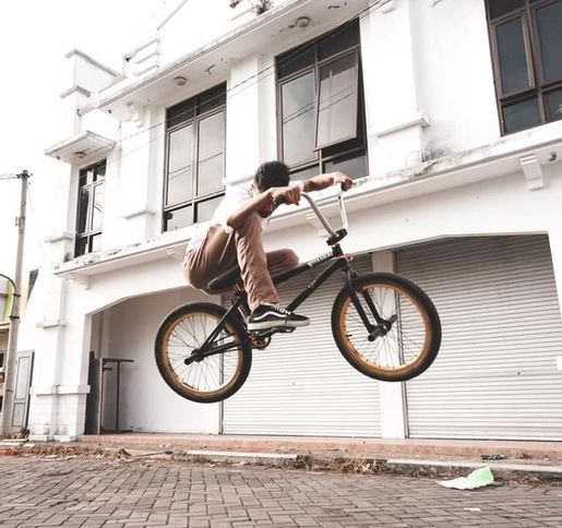 man in white t-shirt and brown trousers mid jump on a bmx