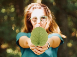 a women outside in the sun wearing glasses holding a leaf in front of her